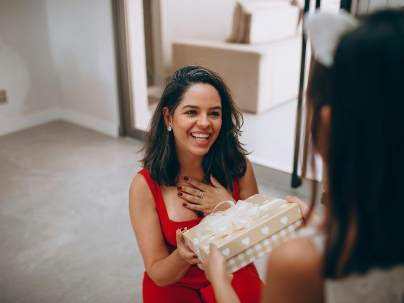 Thoughtful-Christmas-Gifts-For-Parents-That-They-Will-Love-this picture-shows-a daughter-giving-a-gift-to-her-mother-who-is- seen-smiling